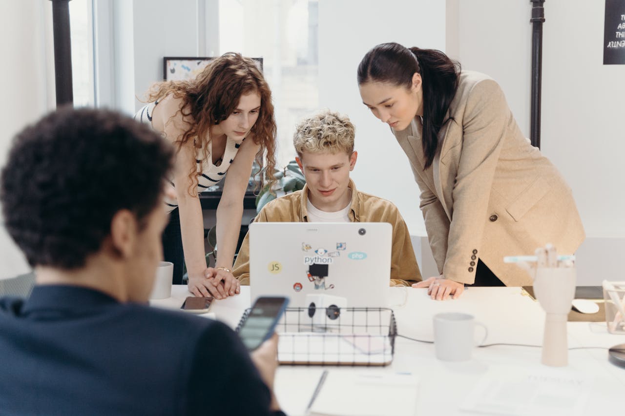 Three colleagues collaborate on a laptop, embodying teamwork and creativity in a modern office environment.